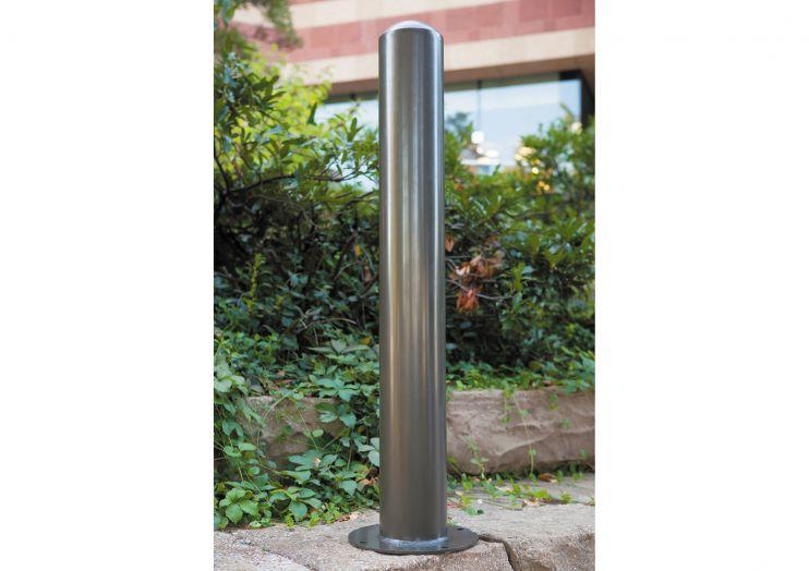 Newport 6" Round Bollard set of 2 in powder-coated steel, sleek cylindrical design, outdoor setting with greenery and building backdrop