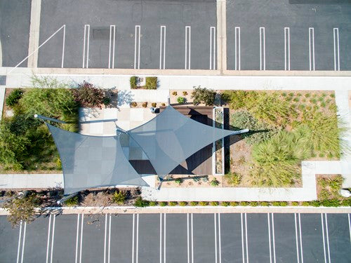 Overhead view of a hyperbolic fabric sail shade stretched between four varying-height columns in a landscaped outdoor area