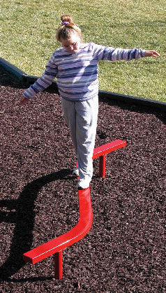 Child balancing on bright red curved playground balance beam over mulch surface