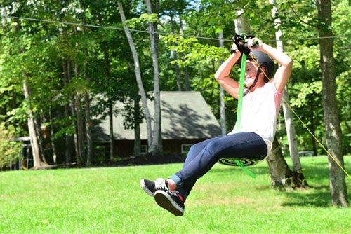 Alien Flier X3 Zip Line Base Kit with rider on disc seat zip lining through green wooded backyard