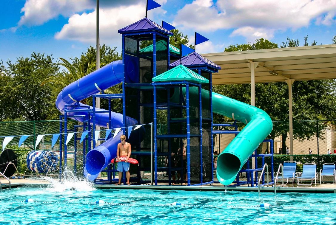 Two curved blue and teal water slides with metal framework and mesh safety netting at a poolside setting