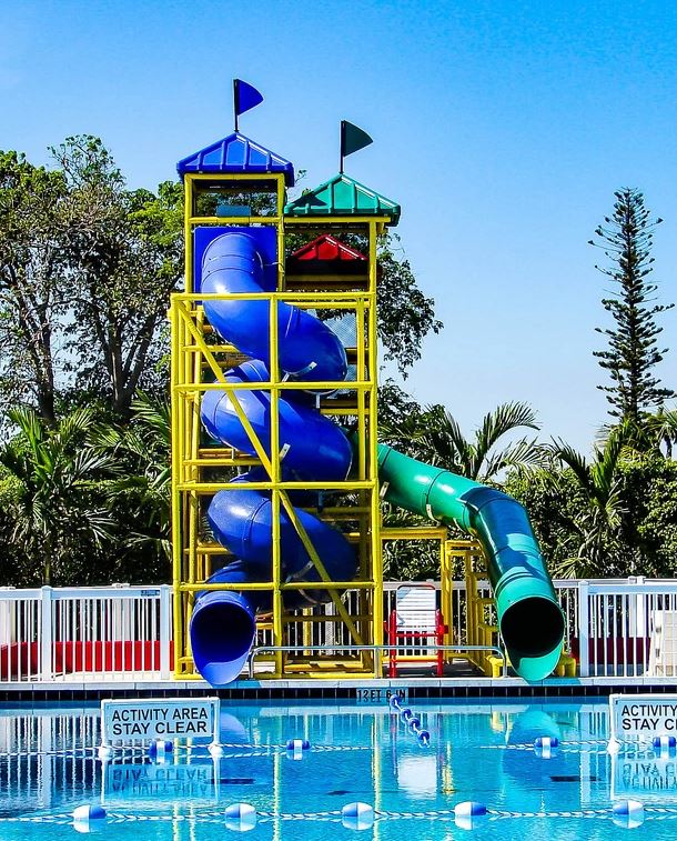 Two colorful water slides with spiral and curved flumes, yellow metal frame, blue and green roofs, beside a pool with safety signs