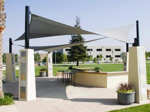 Hyperbolic fabric sail shade stretched between four tall black columns over outdoor seating area