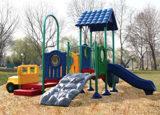 Colorful early childhood playground with climbing rock wall, slides, interactive play panels, and yellow jeep-themed structure on mulch ground