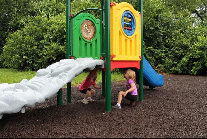 Early childhood playground with dinosaur fossil climber, colorful activity panels, and blue slide on mulch surface