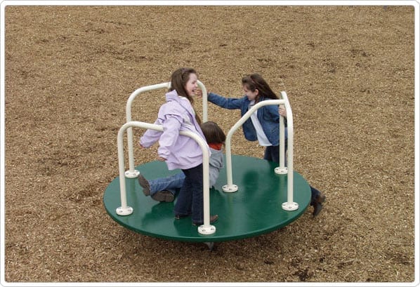 Children playing on a green powder-coated steel merry go round with white handrails on wood chip playground surface