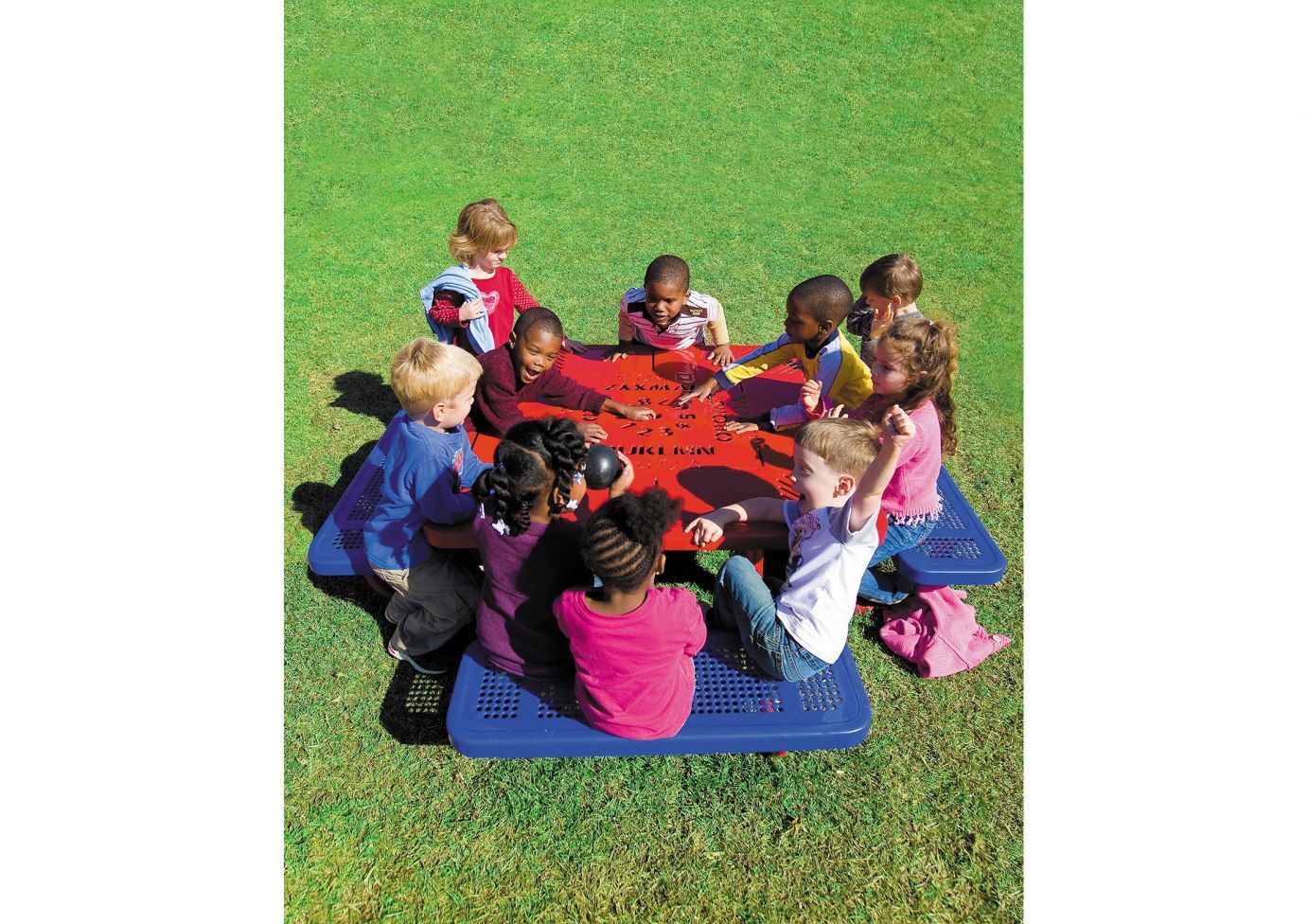 Octagonal red preschool table with alphabet and number cutouts, surrounded by children seated on blue benches outdoors