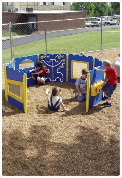 Colorful outdoor playground with interactive sensory panels, spinner maze, and children playing on wood chip ground.