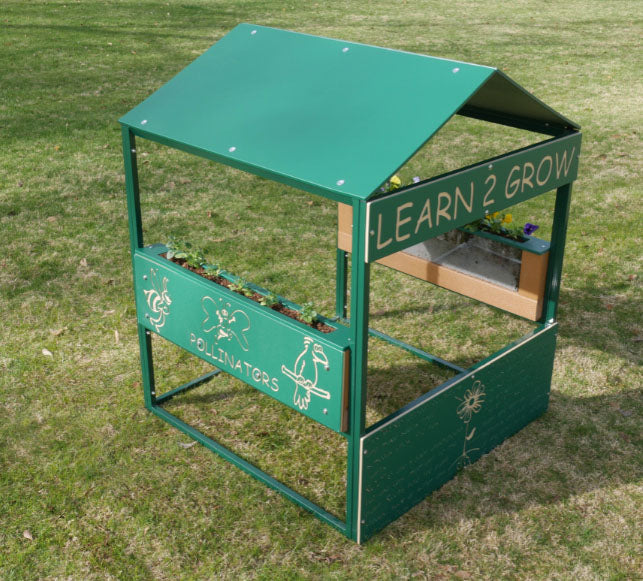 Green outdoor playhouse with clear root view planters and pollinator illustrations on grass, promoting gardening and nature learning.