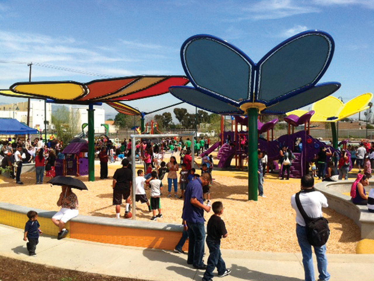 Custom Nature Shade Structure with colorful flower-shaped shade sails over a busy playground on a sunny day