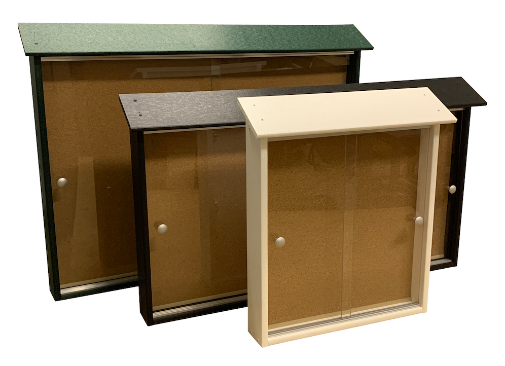 Three outdoor bulletin boards with sliding glass doors and cork surfaces in black, white, and green frames, angled view.