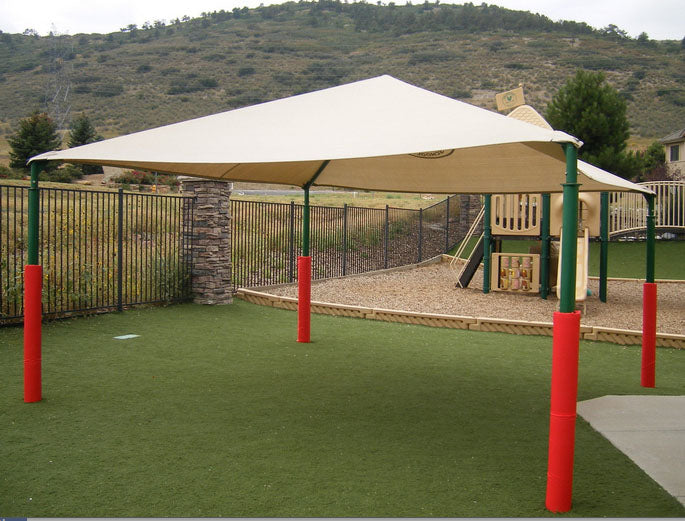 Red wrap-around safety pole pads on green metal poles supporting a beige shade canopy at a playground with artificial turf and play structures