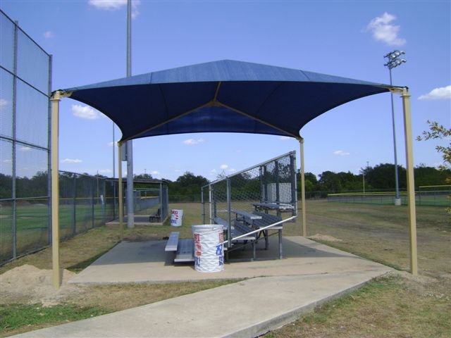Rectangular hip roof shade structure with four posts covering metal bleachers at a sports field, UV-blocking fabric, durable steel frame