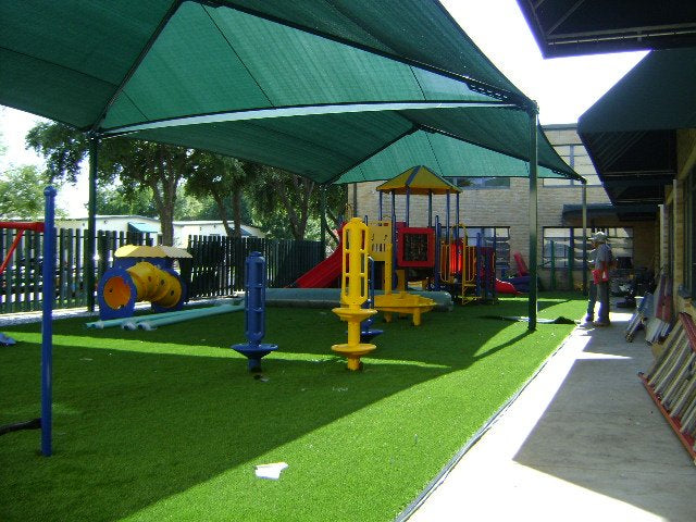 Rectangular hip roof shade structure with four posts covering colorful playground equipment on artificial turf, UV-blocking fabric