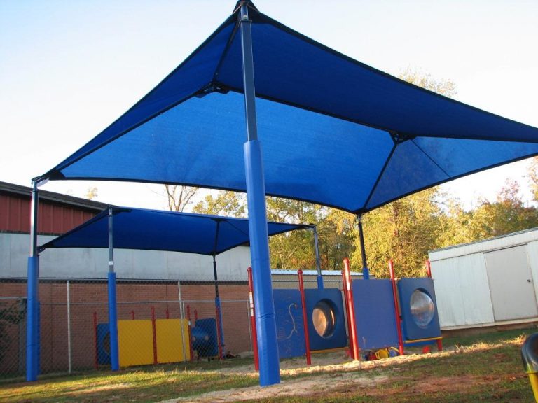 Blue hip roof shade structure with four padded steel posts covering playground panels with circular and rectangular features