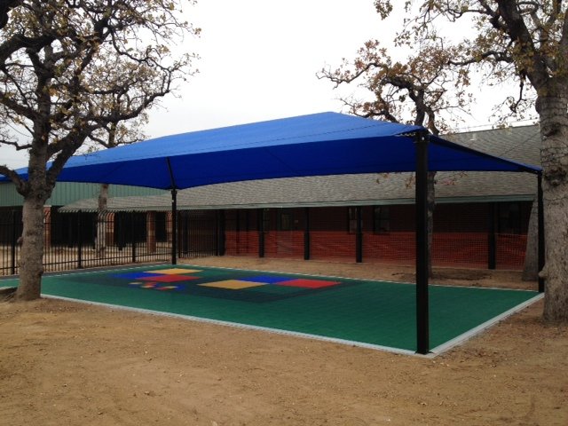Rectangular blue hip roof shade structure with four black posts over colorful playground surface outdoors