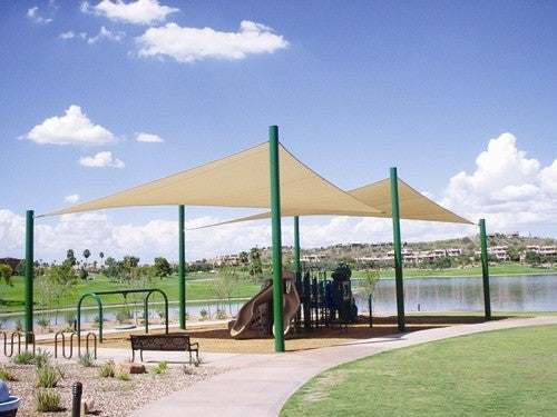 Beige 4-point hypar sail shade with green columns over playground near lake under clear blue sky