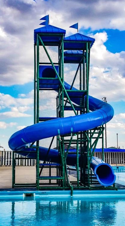 Tall blue spiral water slide with dual towers and safety netting beside a pool under a partly cloudy sky