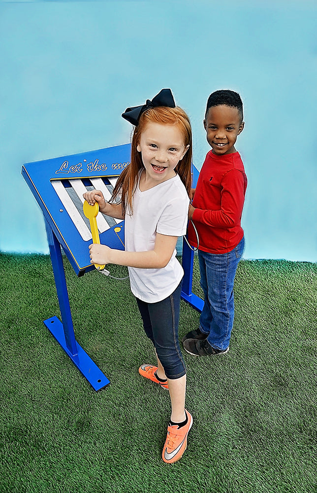 Two children playing a colorful outdoor freestanding xylophone with attached yellow paddles on artificial grass