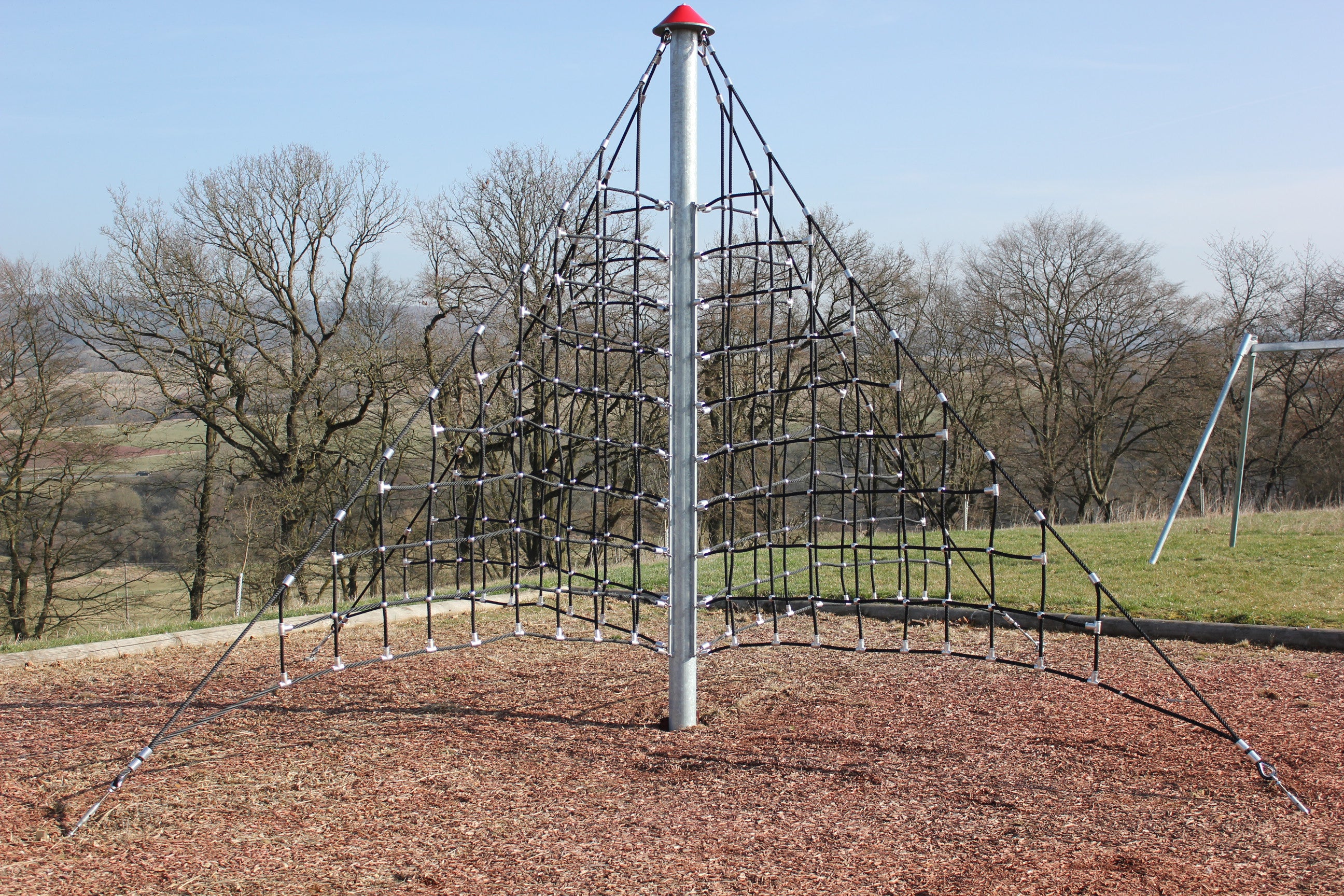 Three-sided pyramid climbing structure with black Netform™ ropes anchored on wood chips, designed for outdoor play and dexterity.