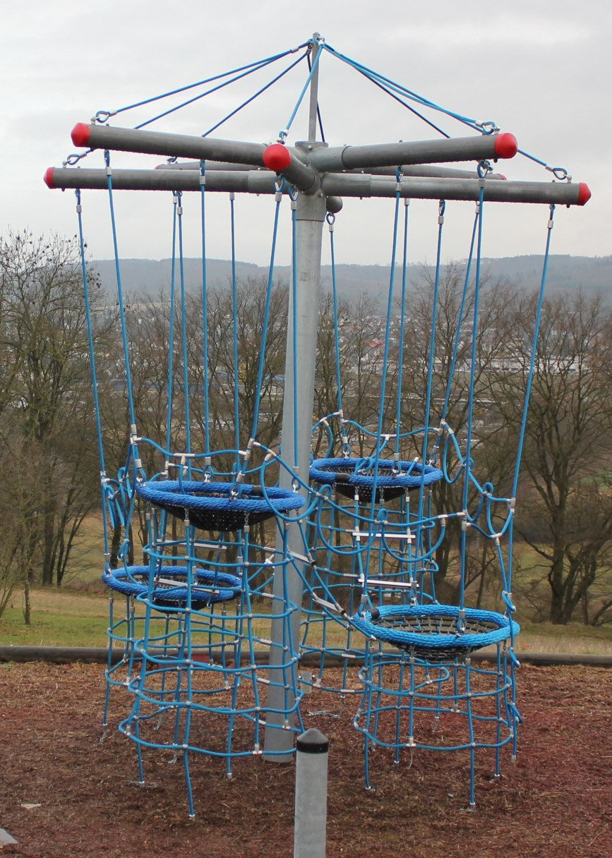 Playground climbing structure with blue rope nets and circular platforms suspended from a central metal pole.