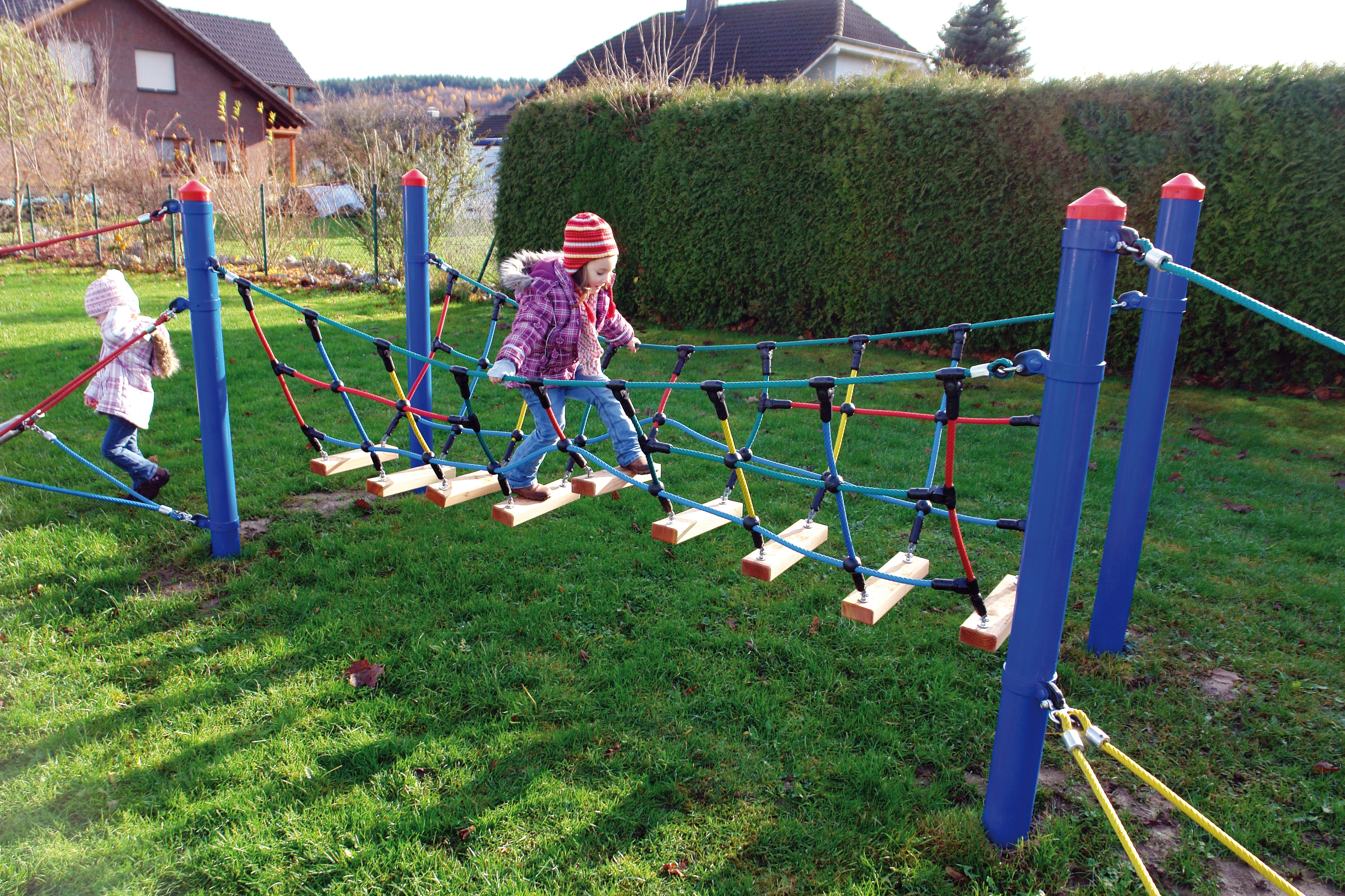 Children crossing colorful rope and wood catwalk bridge playground climbing equipment outdoors