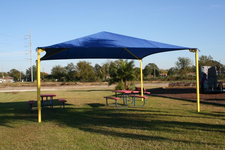 Pyramid-shaped blue canopy shade structure with yellow posts over picnic tables in a park setting