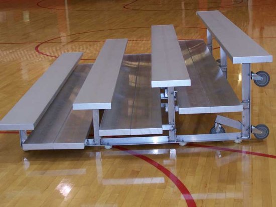Aluminum low-rise bleachers with three rows, tip-and-roll casters, anodized finish, on gym floor