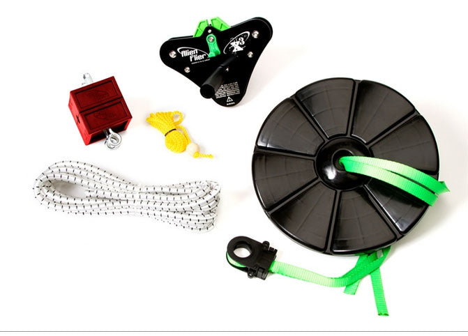 Black anodized aluminum zip line trolley with red locking block, coiled steel cable reel with green strap, yellow and white ropes, and tensioning hardware.