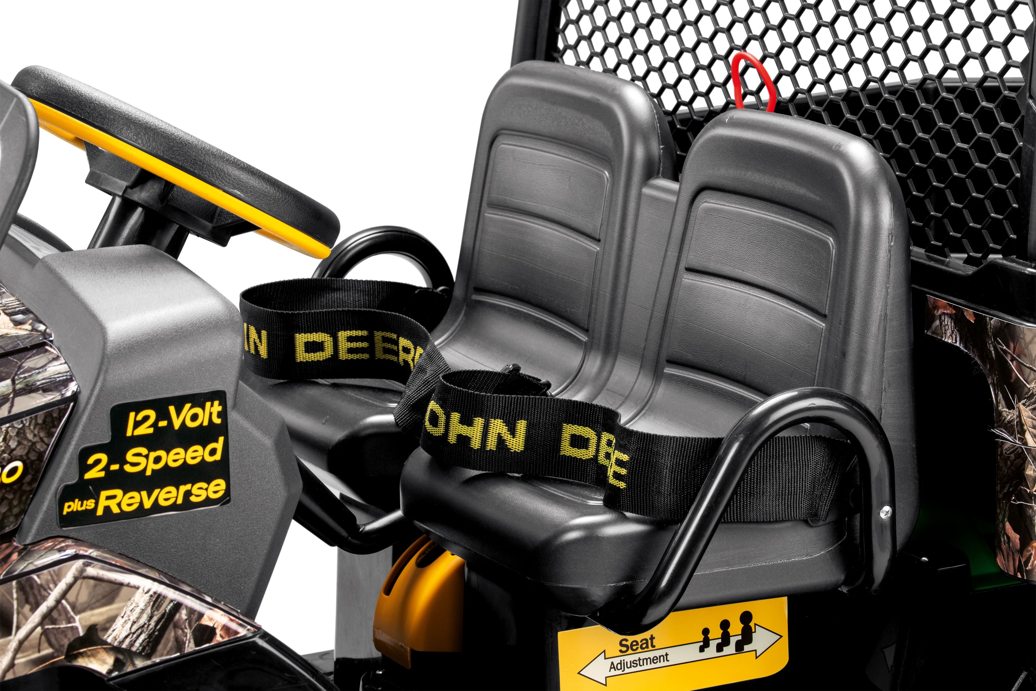 Two black plastic seats with yellow-accented steering wheel, black safety belts, and camouflage details on a ride-on vehicle with a front brush guard and large dump bed.