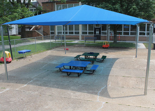 Pyramid Shade Structure with 4 posts in blue over picnic tables on playground concrete, providing UV protection and cooling shade