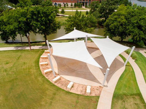 Four-point hypar sail shade with hyperbolic fabric shape supported by tall white columns over circular paved area