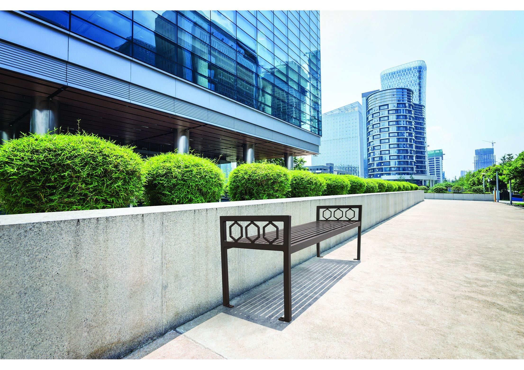 Modern outdoor metal bench with hexagonal geometric side panels along a concrete urban plaza wall
