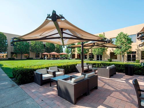 Cantilever single post shade structure with beige fabric canopy over outdoor wicker seating on paved patio in landscaped courtyard
