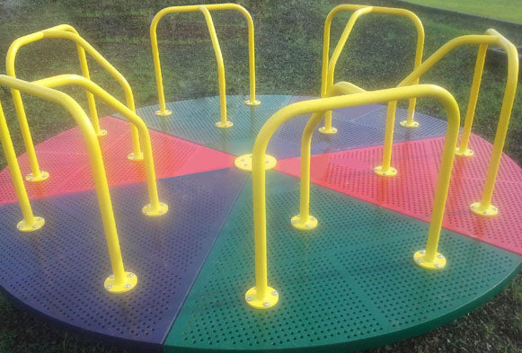 Colorful round playground merry-go-round with yellow handrails and perforated steel deck sections in green, red, and purple