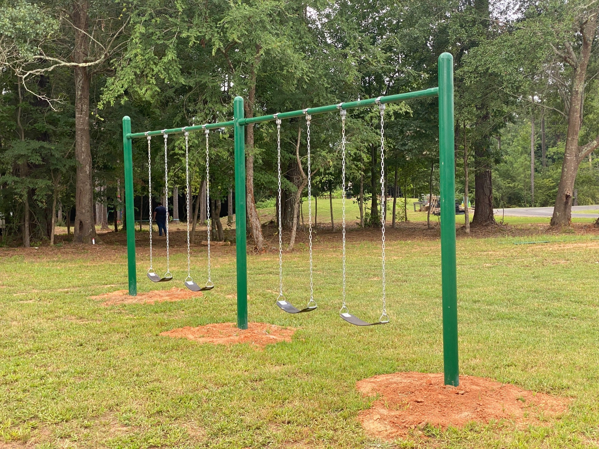 Green metal single-post swing set with six black belt swings on chains in a grassy park setting