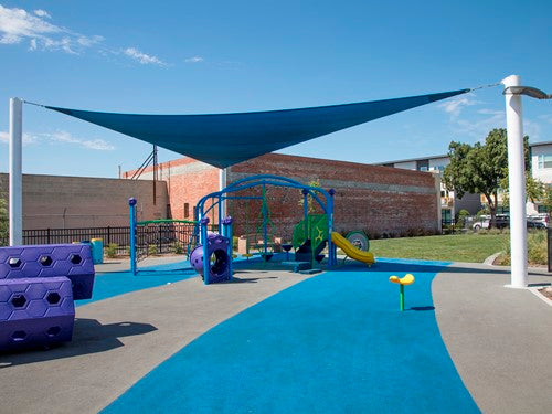 3 Point Sail Shade Structure with triangular blue shade sail over playground climbing and slide equipment in park setting