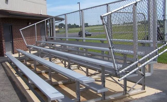 Five-row aluminum bleachers with anodized seats, chain-link guardrails, handrails, and riser planks in outdoor setting