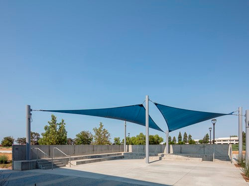 Blue 4-point hypar sail shade with high and low columns creating angled sun protection over concrete seating area