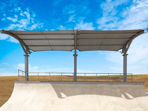 Cantilever shade structure with arched roof over skatepark ramp and metal railing under blue sky