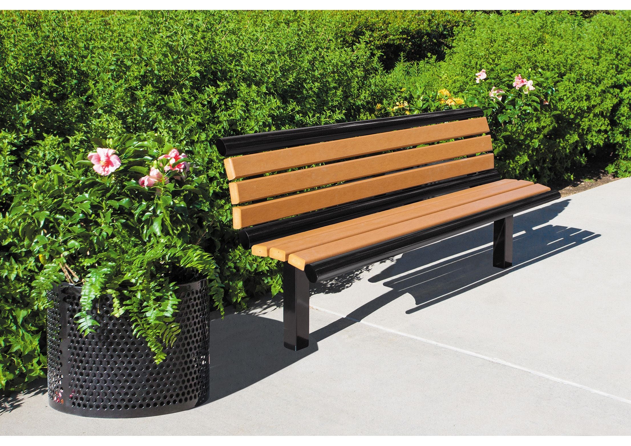 Outdoor recycled plastic bench with black metal frame and backrest beside black metal planter with green plants and pink flowers