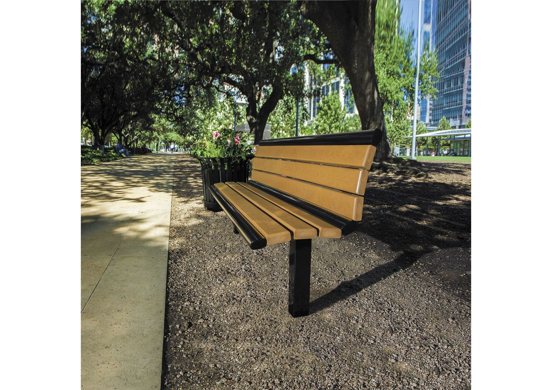 Outdoor bench with tan recycled plastic planks and black metal frame on gravel near tree-lined urban walkway