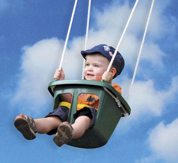 Toddler wearing blue cap and orange shirt secured in green infant bucket swing with safety harness against blue sky with clouds