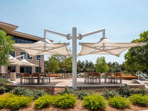 Cantilever single post shade structure with two beige fabric canopies over outdoor seating in landscaped park setting