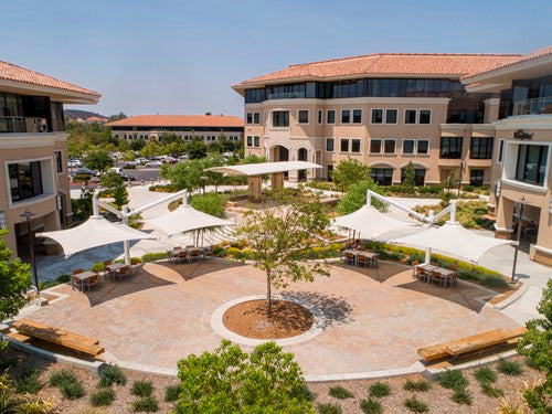 Cantilever single post shade structure with white fabric canopy over outdoor seating in landscaped courtyard
