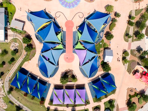 Overhead view of colorful triangular shade sails arranged in butterfly shape over playground with multiple columns