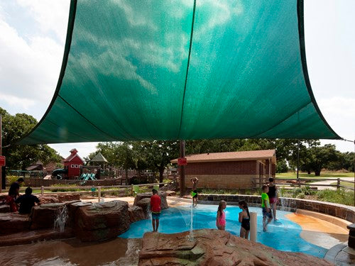 Green 4-point hypar sail shade with hyperbolic shape over splash pad featuring children playing and water features