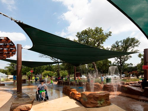 Dark green 4-point hypar sail shade over splash pad with water fountains and children playing