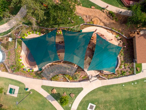 Overhead view of three teal 4-point hypar sail shade structures with varying column heights creating hyperbolic shapes over a park area