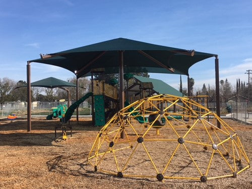 Single post pyramid cantilever shade with dark green fabric over playground slides and climbing dome